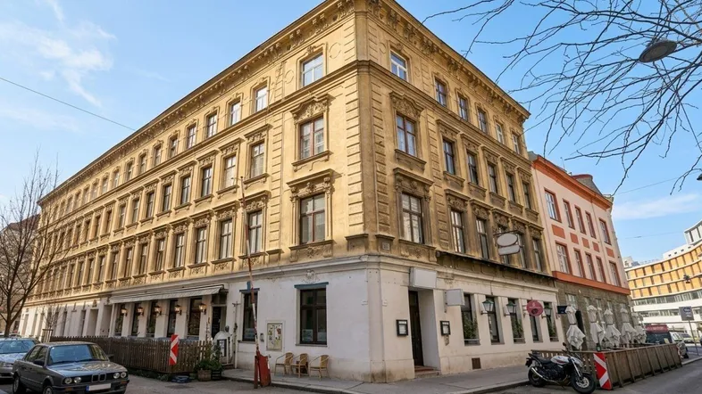 Historisches Eckgebäude mit reich verzierter Fassade und Geschäften im Erdgeschoss in urbaner Umgebung.