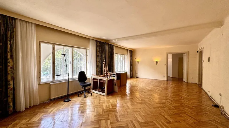 Geräumiges Wohnzimmer mit Fischgrätparkett, hohen Fenstern und viel Tageslicht.