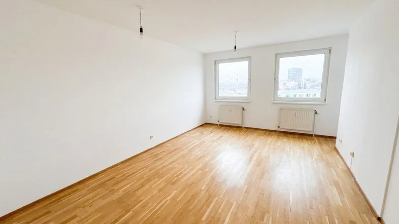 Helles Zimmer mit Parkettboden, weißen Wänden und Blick auf die Stadt.