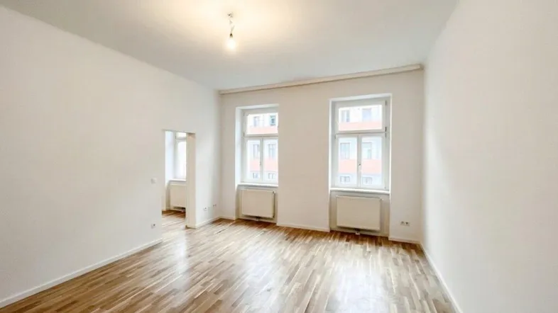 Helles, leeres Zimmer mit Parkettboden und zwei Fenstern, bereit zur individuellen Gestaltung.
