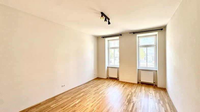 Helles Zimmer mit Parkettboden, weißen Wänden und zwei Fenstern, ideal als Wohn- oder Schlafzimmer.