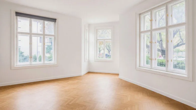 Helles, leeres Zimmer mit Fischgrätparkett und großen Fenstern, die viel Tageslicht hereinlassen.