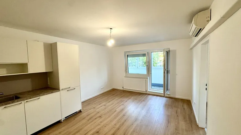 Helles Wohnzimmer mit integrierter Küchenzeile, Laminatboden und Zugang zum Balkon.