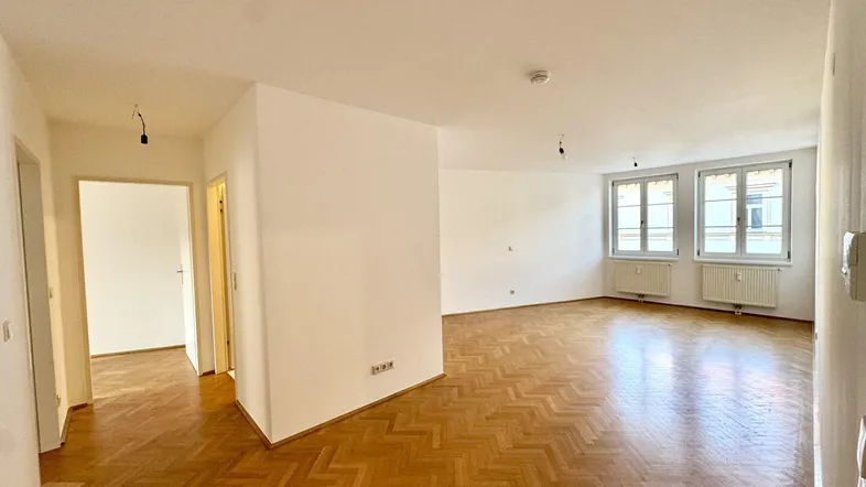 Helles, leeres Wohnzimmer mit Fischgrätparkett und mehreren Fenstern, bereit zur individuellen Gestaltung.