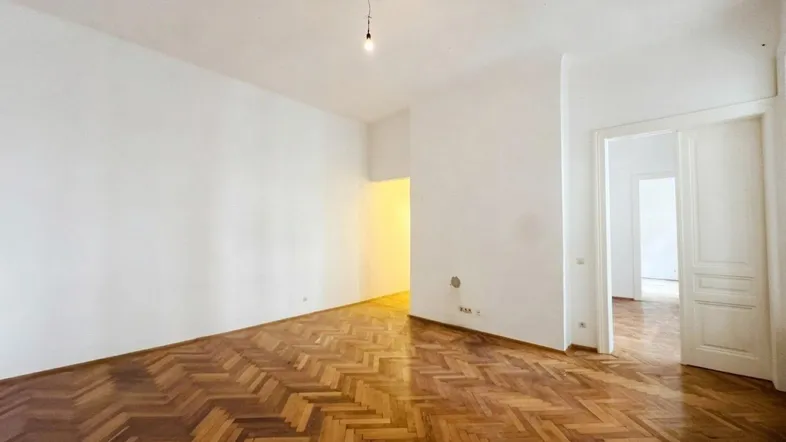 Geräumiges, leeres Zimmer mit Fischgrätparkett und Zugang zu weiteren Räumen.
