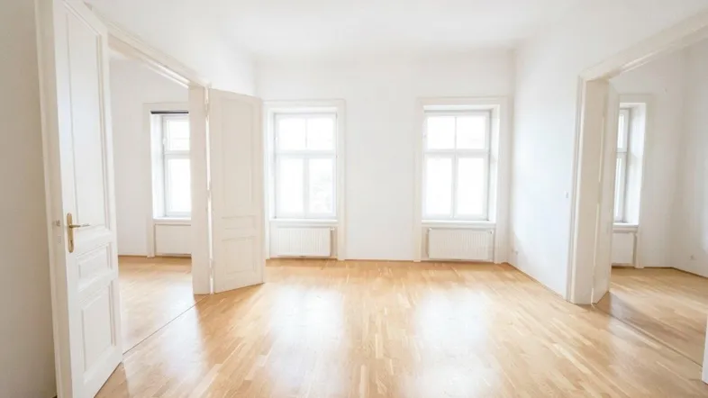 Helles, leeres Zimmer mit Parkettboden und hohen Fenstern, bereit zur individuellen Gestaltung.