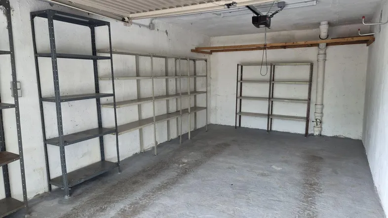 Geräumige Garage mit praktischen Metallregalen und Betonboden für Lagerzwecke.