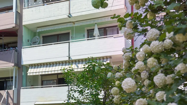 Mehrfamilienhaus mit mehreren Balkonen und grüner Umgebung an einem sonnigen Tag.