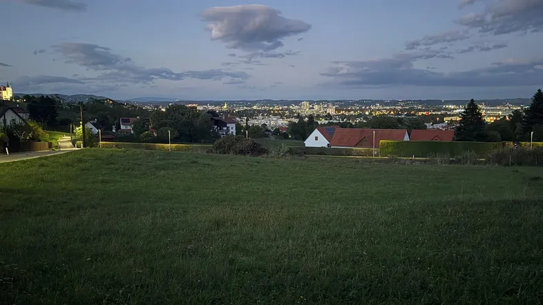 Weitläufiges Feld im Vordergrund mit Blick auf die beleuchtete Stadt bei Dämmerung.