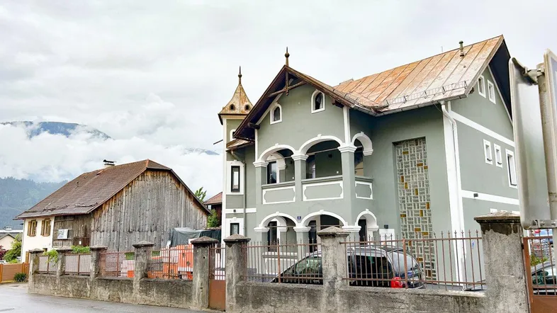 Historisches Gebäude mit markanter Architektur und Bergblick, umgeben von einer Steinmauer.