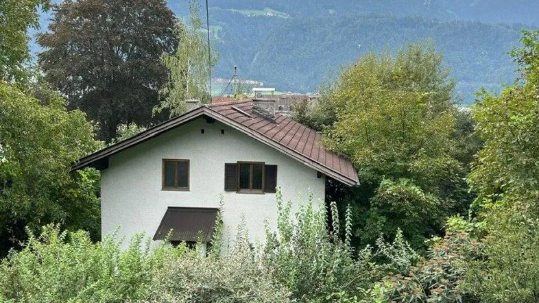 Einfamilienhaus umgeben von üppigem Grün mit Bergblick unter bewölktem Himmel.