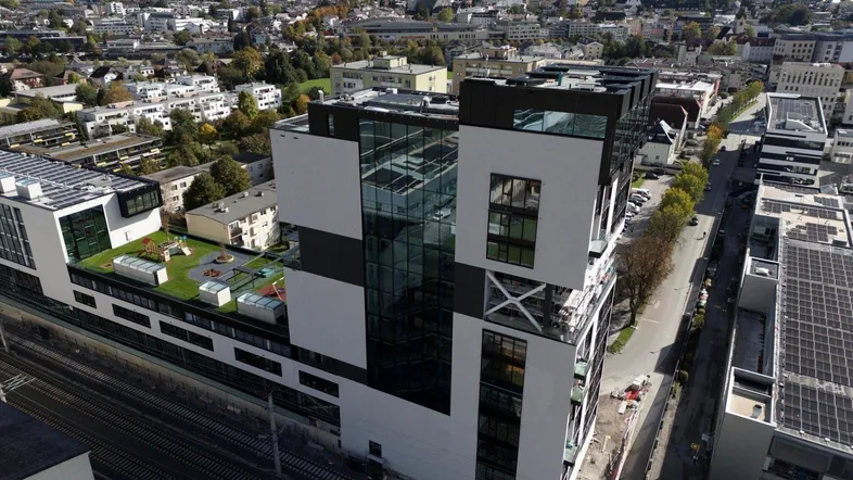 Moderne Architektur eines Gebäudekomplexes mit Glasfassaden und begrüntem Dach in städtischer Umgebung.