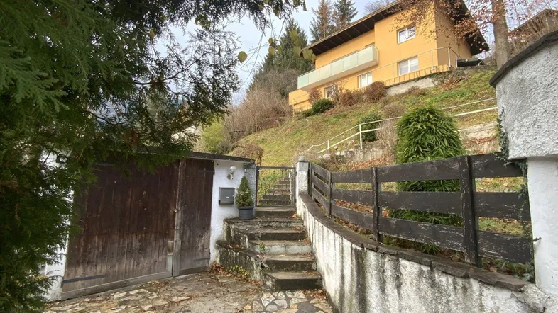 Haus auf Hanglage mit Garage, Steintreppe und umgebender Vegetation.