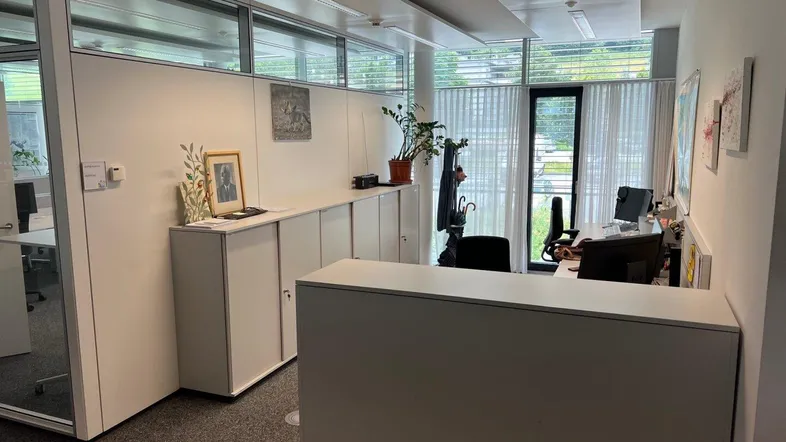 Modernes Büro mit großen Fenstern, viel Tageslicht und funktionalen Möbeln für eine angenehme Arbeitsatmosphäre.