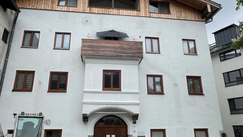 Fassade eines modernen Gebäudes mit Holzelementen im Dachbereich und einem Bagger davor.