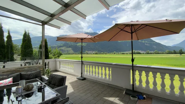 Gemütliche überdachte Terrasse mit Loungemöbeln und weitem Blick über grüne Felder und Berge.