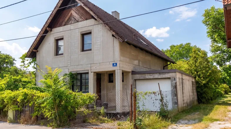 Altes Einfamilienhaus mit Satteldach und angrenzender Garage, umgeben von viel Grün.