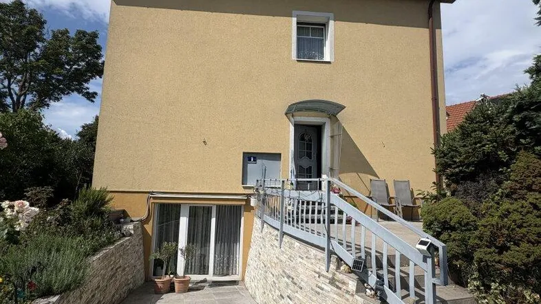 Gelbe Hausfassade mit Eingangsbereich, Treppe und Rampe unter blauem Himmel.