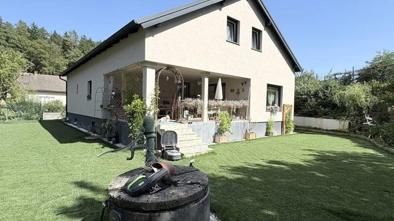 Gepflegter Garten mit Rasenfläche, altem Brunnen und überdachter Terrasse am Haus.