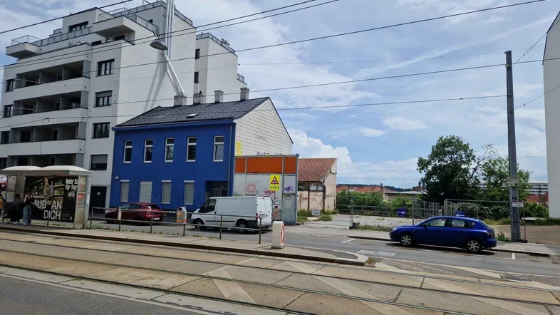 Straßenansicht mit einem blauen Gebäude und einem modernen Apartmentkomplex im Hintergrund.