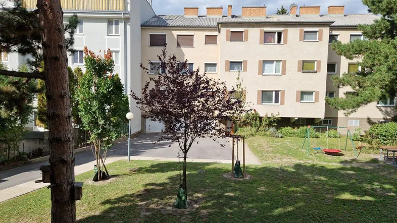 Blick auf den gepflegten Innenhof mit Grünflächen, Bäumen und einem kleinen Spielplatz zwischen den Wohngebäuden.