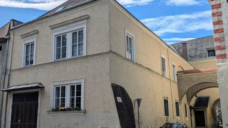 Historisches Gebäude mit heller Fassade und Durchgang zu einem Innenhof oder einer Gasse.