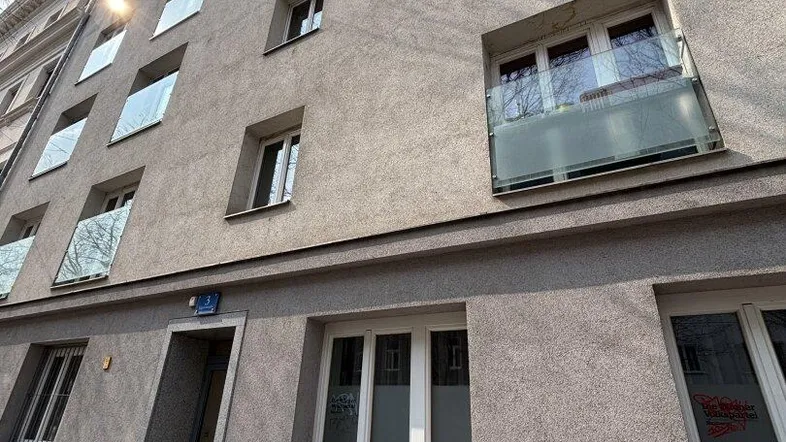 Graue Fassade eines Mehrfamilienhauses mit vielen Fenstern und kleinen französischen Balkonen unter blauem Himmel.