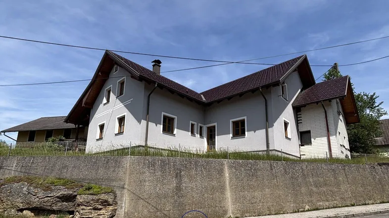 Ländliches Einfamilienhaus mit Satteldach und grauer Fassade, umgeben von grüner Natur.