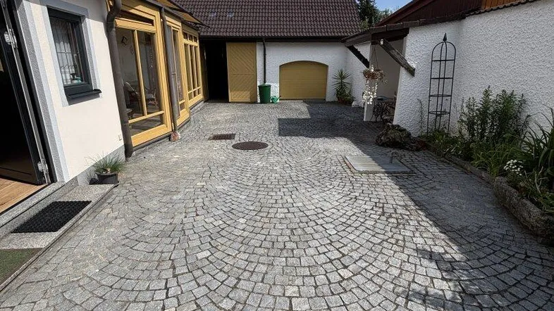 Gepflasterter Innenhof mit Zugang zu verschiedenen Gebäudeteilen unter blauem Himmel.