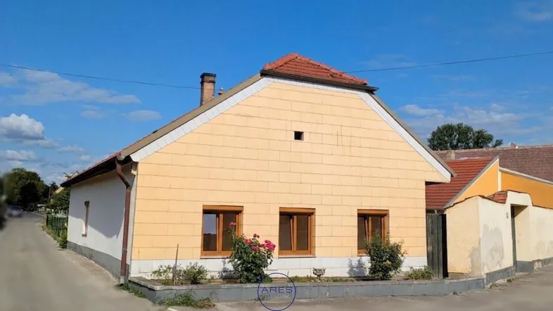 Gelbe Hausfassade mit rotem Ziegeldach und kleinen Fenstern von der Straße aus gesehen.