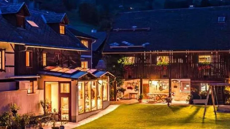 Abendliche Ansicht des Anwesens mit beleuchtetem Garten, Wintergarten und gemütlicher Sitzgruppe im Freien.