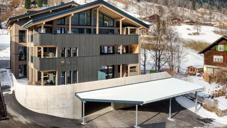 Modernes Gebäude mit Holzfassade und Carport in verschneiter Berglandschaft.
