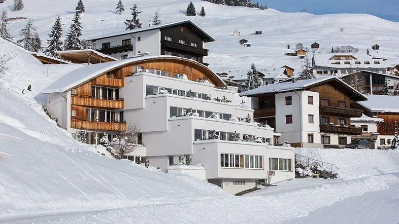 Modernes Aparthotel mit Terrassen und Balkonen, eingebettet in eine verschneite Berglandschaft.