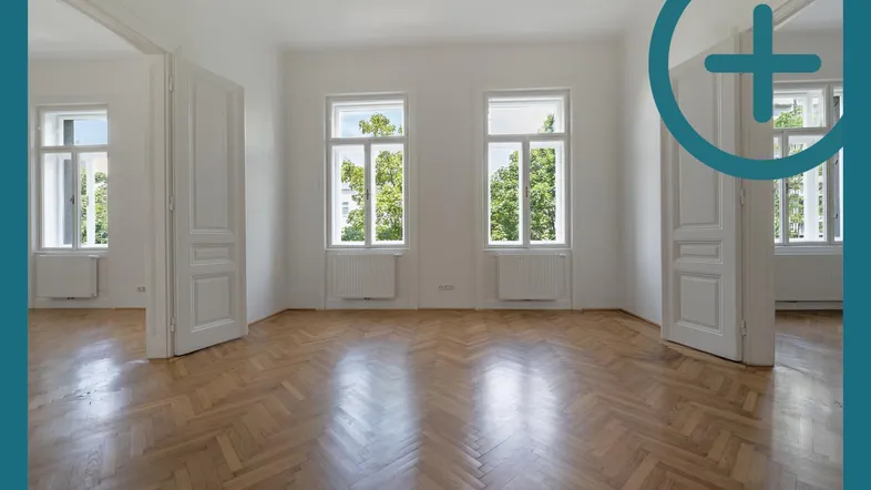 Helles Zimmer mit Fischgrätparkett und hohen Fenstern, das viel Tageslicht hereinlässt.