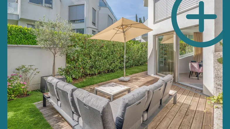 Gemütliche Holzterrasse mit Loungemöbeln und Sonnenschirm, umgeben von einer grünen Hecke.
