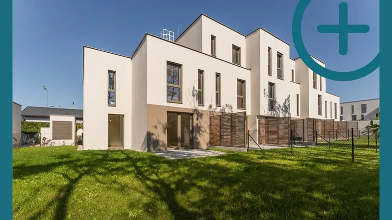 Moderne Reihenhäuser mit weißer Fassade und großem Gartenbereich unter blauem Himmel.