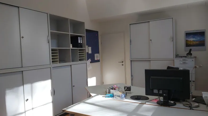 Geräumiges Büro mit hellen Schränken, viel Stauraum und natürlichem Lichteinfall durch die Fenster.