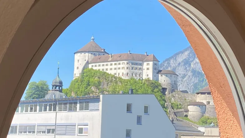 Malerischer Blick durch ein Bogenfenster auf eine historische Burg auf einem Hügel und Berge.