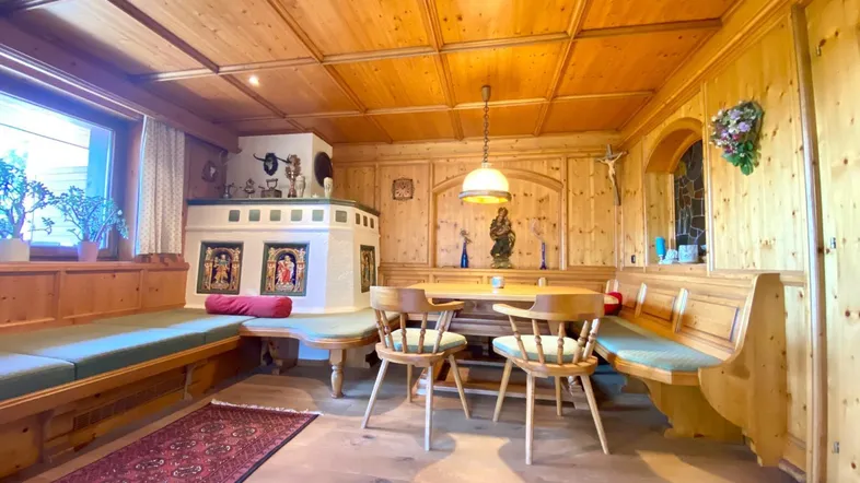 Gemütlicher Essbereich im alpinen Stil mit Holztäfelung, Kachelofen und traditionellen Sitzbänken.