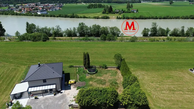 Luftaufnahme eines Hauses mit angrenzendem Grundstück, Fluss und Bergpanorama im Hintergrund.