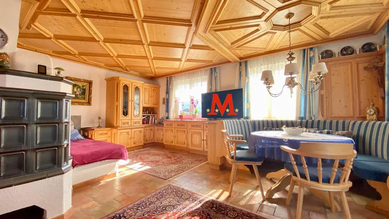 Gemütliches Wohnzimmer im alpinen Stil mit Holzbalkendecke, Kachelofen und Essecke.