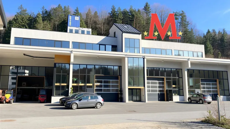 Modernes Geschäftsgebäude mit großen Glasfronten und einem markanten roten Logo vor bewaldeter Bergkulisse.