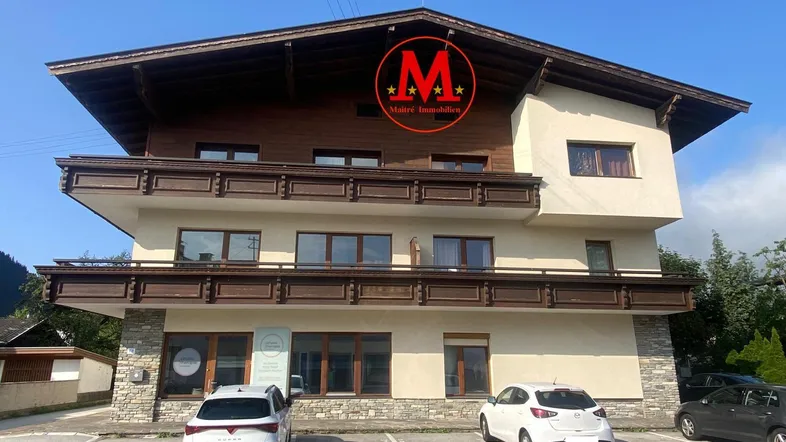 Mehrfamilienhaus im alpinen Stil mit Holzverkleidung, Steinakzenten und Balkonen, umgeben von Bergen.