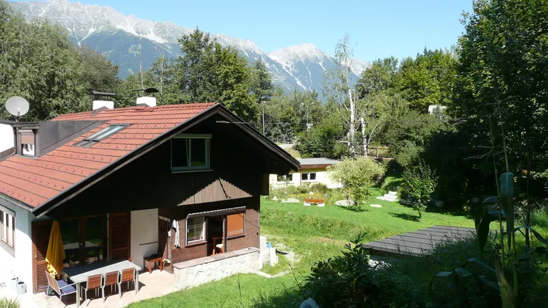 Charmantes Haus mit Terrasse und Bergblick, umgeben von grüner Natur und Bäumen.