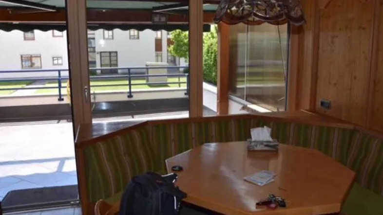 Traditioneller Essbereich mit Holztisch und gepolsterter Eckbank, mit Zugang zu einem Balkon und Blick ins Grüne.