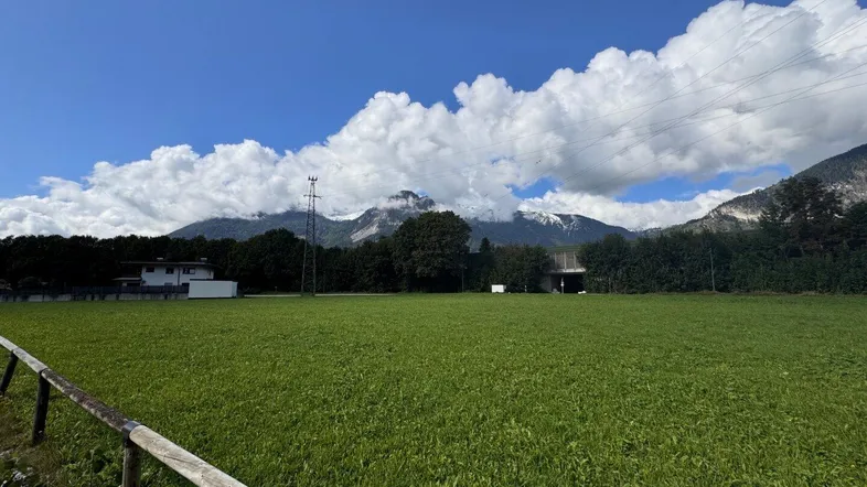 Weitläufige grüne Wiese mit majestätischen Bergen im Hintergrund unter einem strahlend blauen Himmel.