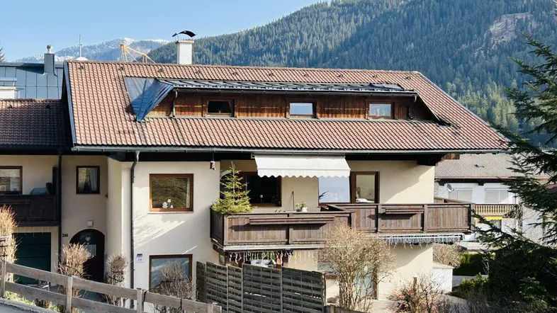 Charmantes Haus in den Bergen mit traditionellem Ziegeldach und Balkonen, umgeben von grüner Natur.