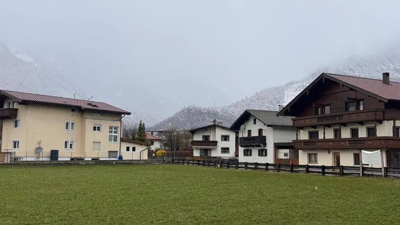 Blick auf traditionelle Häuser in einer ländlichen Umgebung mit schneebedeckten Bergen im Hintergrund.