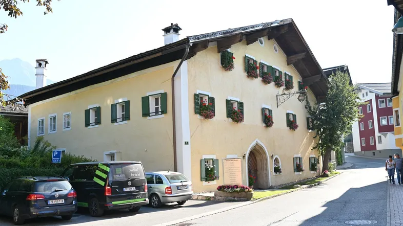 Traditionelles Gebäude mit gelber Fassade, grünen Fensterläden und Blumenkästen an einer Straße.