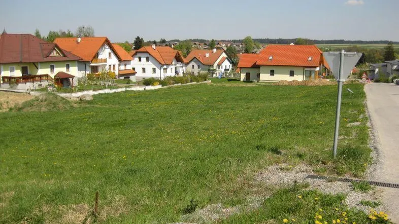 Grünfläche mit Blick auf umliegende Wohnhäuser in ländlicher Umgebung unter blauem Himmel.